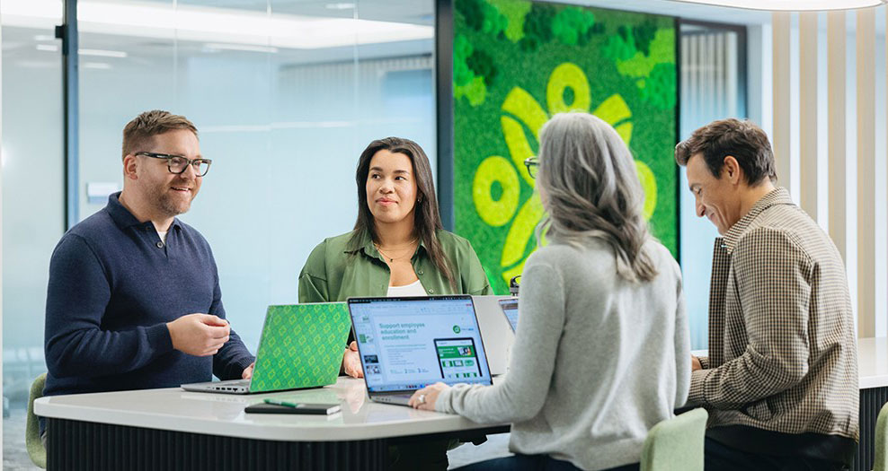 Group of Securian Canada employees chat during a meeting with laptops open in front of them.