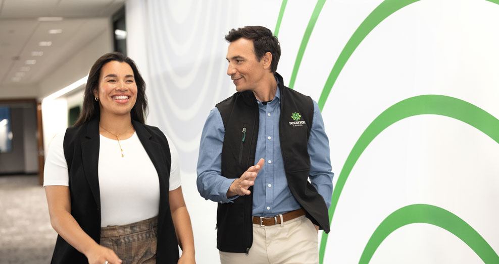 Two young professionals walking on a bright hallway smiling.