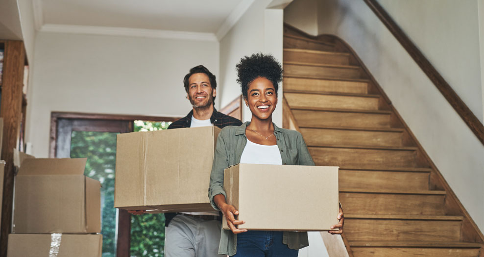Couple carries moving boxes into a new home.