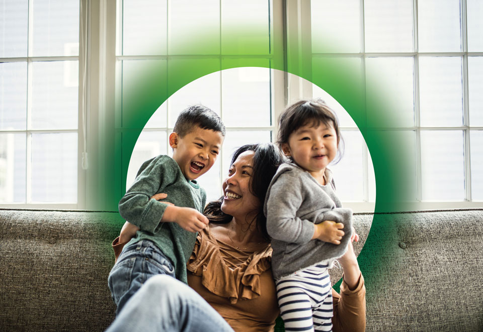 Adult with two children smiles on a couch surrounded by a graphic green halo.